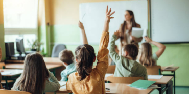 Students raising hands while teacher asking them questions in classroom