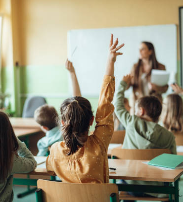 Students raising hands while teacher asking them questions in classroom